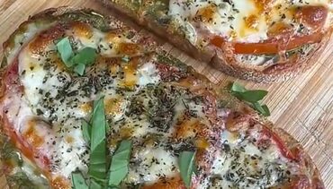 Twee Caprese toasts met gesmolten mozzarella, tomaat, pesto en verse basilicum op een plank