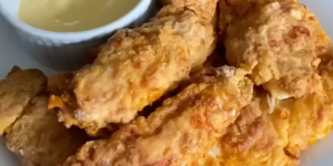 Krokante chicken tenders met een romige dipsaus op een wit bord