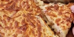 Goudbruine broodtaart met ham en kaas, in punten gesneden op een houten plank
