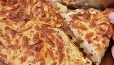 Goudbruine broodtaart met ham en kaas, in punten gesneden op een houten plank