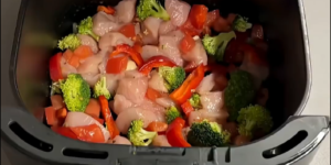 Kipfilet, broccoli, paprika en tomaat in de mand van een Airfryer voor het bakken