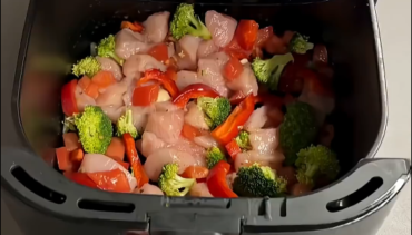 Kipfilet, broccoli, paprika en tomaat in de mand van een Airfryer voor het bakken