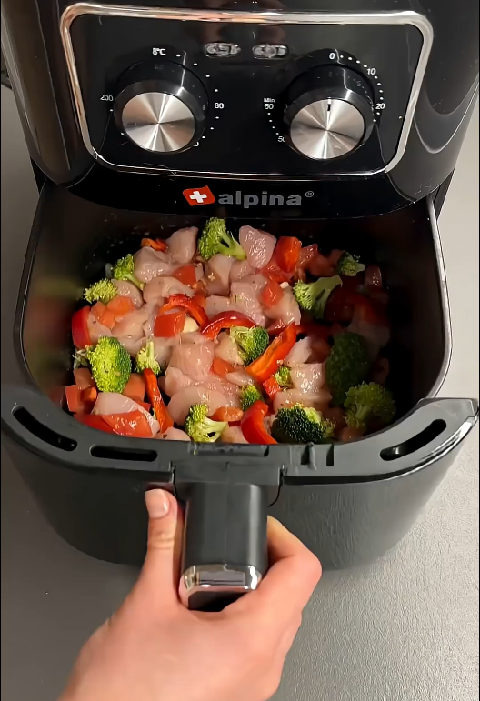 Kipfilet, broccoli, paprika en tomaat in de mand van een Airfryer voor het bakken